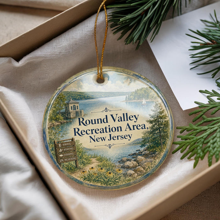 A round ornament with a scenic landscape of a river, mountains, and a small building, hanging from a string.
