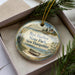 A decorative ornament with a lighthouse and a boat, placed in a box with pine branches.