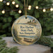 A round ornament with a lighthouse and a boat on the water, surrounded by greenery and a string of lights.
