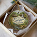 A decorative ornament in a box, featuring a scenic landscape with a house, a waterfall, and a bridge.