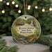 A round ornament with a painting of a house and a waterfall, surrounded by greenery, hangs in front of a blurred background with twinkling lights.