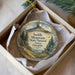 A decorative ornament in a box, featuring a scenic landscape with a mountain, trees, and a bird.