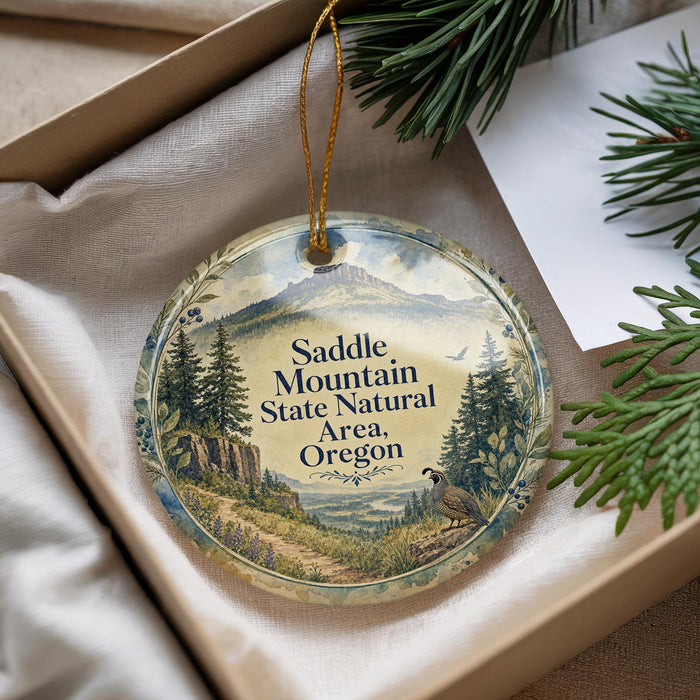 A decorative ornament with a scenic mountain landscape and pine trees, featuring the text "Saddle Mountain State Natural Area, Oregon".