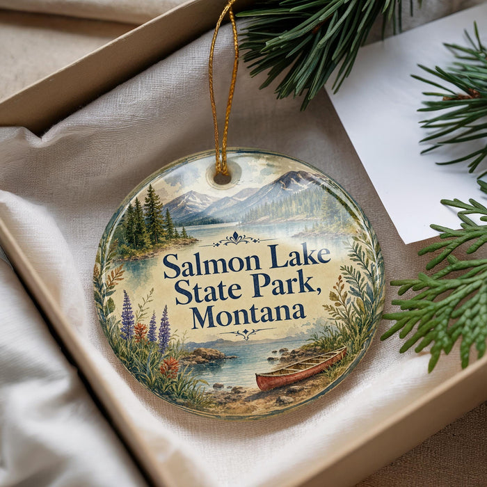 A decorative ornament with a scenic landscape of Salmon Lake State Park, Montana, featuring a lake, mountains, pine trees, and a canoe.