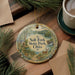A round ornament with a scenic illustration of Salt Fork State Park, Ohio, featuring a deer, a stream, and a waterfall. The ornament is hanging on a wooden surface, surrounded by pine branches and a cup of coffee.