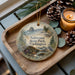 A decorative ornament with a scenic image of Saltwater State Park, Washington, featuring pine cones, a candle, and a bird.