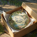 A decorative ornament in a box, featuring a scenic landscape with a waterfall and a cabin, with the text "Sam A. Baker State Park, Missouri" printed on it.