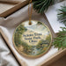 A decorative ornament with a scenic landscape of a river, bridge, and trees, hanging from a string.