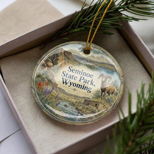 A decorative ornament in a box, featuring a scenic landscape with mountains, a river, and a bighorn sheep.