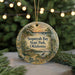 A decorative ornament with a scenic landscape featuring a lake, trees, and a bird, hanging in front of a Christmas tree with twinkling lights.