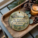 A wooden tray with a decorative ornament featuring a portrait of a man, surrounded by pine cones and a lit candle.
