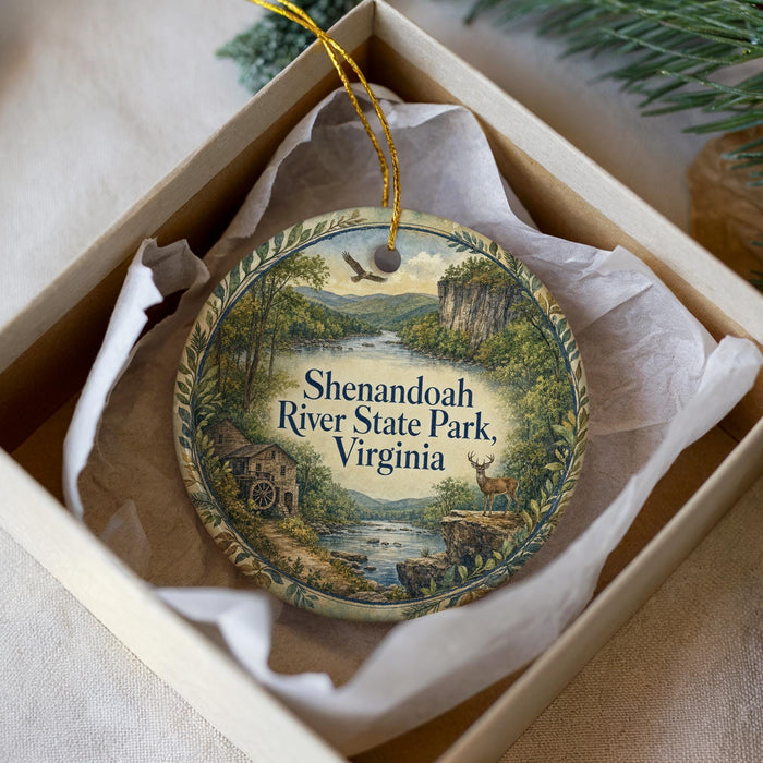 A decorative ornament in a box, featuring a scenic landscape with a river, mountains, and wildlife.