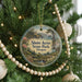 A round ornament hanging on a Christmas tree, featuring a scenic landscape with a lighthouse and a river.