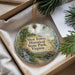 A round ornament with a scenic landscape and text, placed in a box with pine branches.