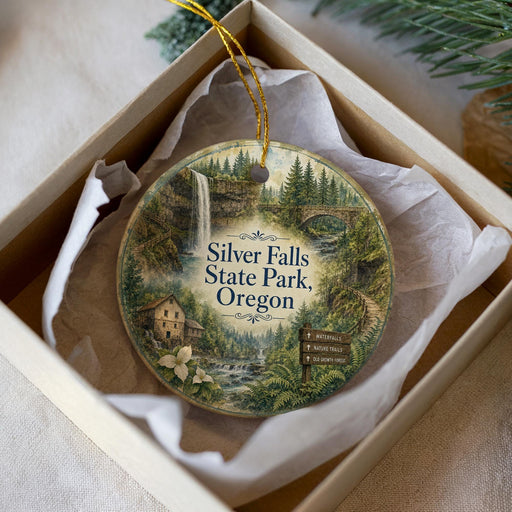 A decorative ornament in a box, featuring a scenic landscape with a waterfall, forest, and a bridge.
