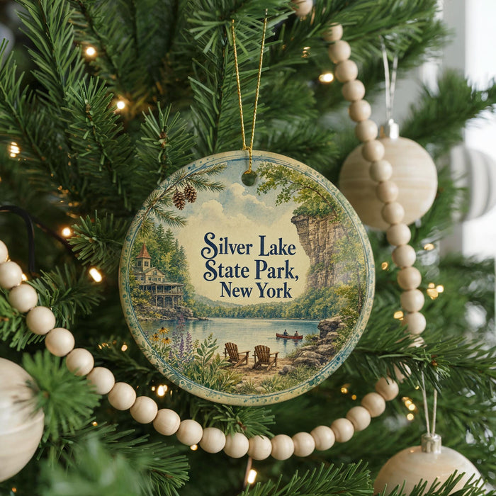 A round ornament hanging on a Christmas tree, featuring a scenic landscape with a lake, mountains, and a cabin.