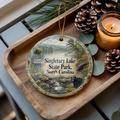 A decorative ornament featuring a scenic image of Singletary Lake State Park, North Carolina, with pine cones and a lit candle on a wooden tray.