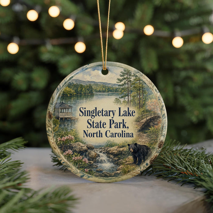 A round ornament with a scenic image of Singletary Lake State Park in North Carolina, featuring a bear in the foreground and a waterfall in the background.