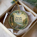A decorative ornament in a box, featuring a scenic landscape with a river, trees, and mountains.