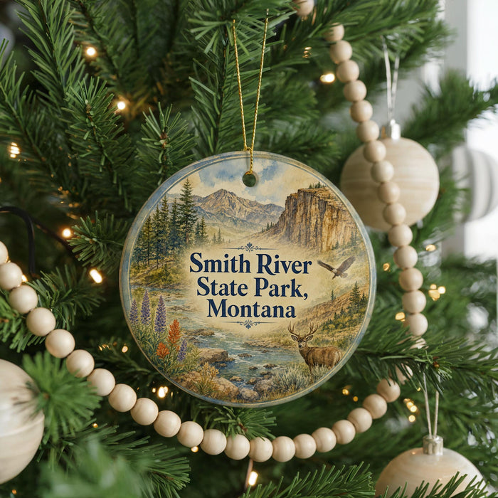 A round ornament hanging on a Christmas tree, featuring a scenic landscape with mountains, trees, and a river.