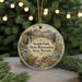 A round ornament with a scenic landscape featuring a waterfall, mountains, and wildlife, including a bird and a deer, is displayed in front of a blurred background with Christmas lights.