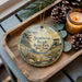 A decorative ornament featuring a beach scene with a lighthouse, pine cones, and a candle on a wooden tray.
