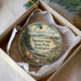 A decorative ornament in a box, featuring a lighthouse and a scenic landscape.