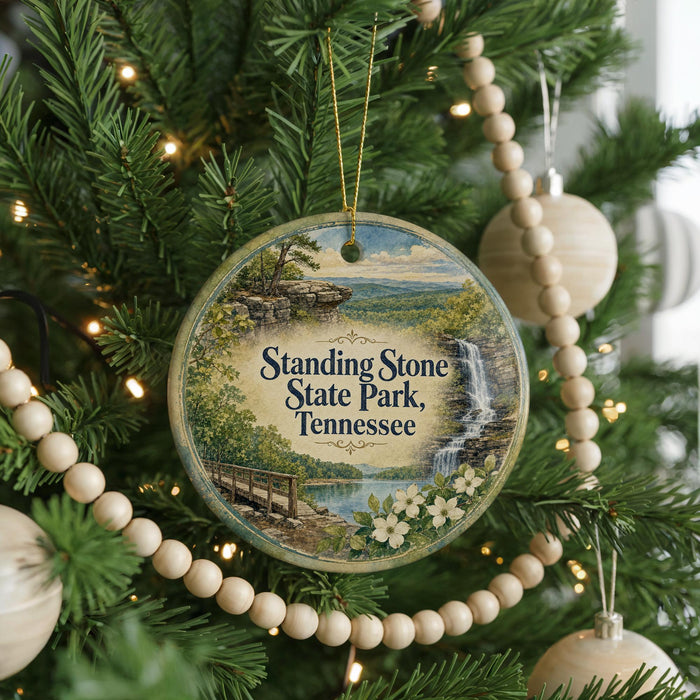 A round ornament hanging on a Christmas tree, featuring a scenic landscape with a waterfall and a bridge.