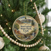 A round ornament hanging on a Christmas tree, featuring a scenic landscape with mountains, a waterfall, and a bridge.