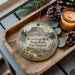 A decorative ornament featuring a scenic image of Steamboat Rock State Park in Washington, accompanied by pine cones and a lit candle on a wooden tray.