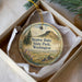 A decorative ornament in a box, featuring a scenic landscape with mountains, trees, and a body of water.