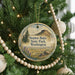 A round ornament hanging on a Christmas tree, featuring a scenic landscape with mountains and pine trees.