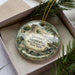 A decorative ornament in a box, featuring a historical scene with a monument and a cannon, along with the text "Steuben Memorial State Historic Site, New York".
