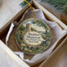 A round ornament with a painting of a historical monument and a statue, placed in a box with tissue paper.