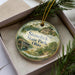 A decorative ornament in a box, featuring a scenic landscape with a bridge and trees, with the text "Stonelick State Park, Ohio" prominently displayed.