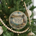 A round ornament hanging on a Christmas tree, featuring a scenic landscape with mountains, a lake, and a bird.