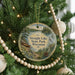 A round ornament hanging on a Christmas tree, featuring a scenic image of a lake surrounded by trees and mountains.