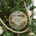 A round ornament hanging on a Christmas tree, featuring a scenic image of a lake and a cabin.