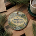 A decorative ornament with a scenic landscape of Susan Creek State Recreation Site, Oregon, featuring a bird and a stream, is displayed on a wooden surface alongside a cup of coffee and some pine branches.