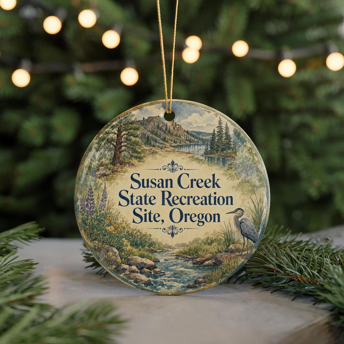 A round ornament with a scenic landscape and text, hanging on a string.