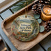 A wooden tray with a decorative ornament featuring a scenic landscape of Talimena State Park, Oklahoma, and pine cones.