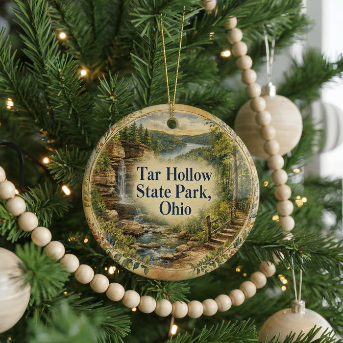 A round ornament hanging on a Christmas tree, featuring a scenic landscape with a waterfall and a path leading to a cliff.