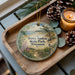A decorative ornament featuring a scenic landscape of Terry Andrae State Park, Wisconsin, with pine cones and a lit candle on a wooden tray.