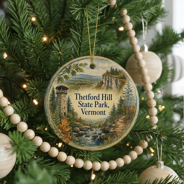 A round ornament hanging on a Christmas tree, featuring a scenic landscape with a tower and a river.