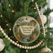A round ornament hanging on a Christmas tree, featuring a scenic landscape with a tower and a river.