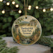 A round ornament with a scenic landscape of a mountain, a tower, and a stream, surrounded by pine trees and a string of lights.