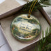 A decorative ornament in a box, featuring a scenic landscape with a lake, forest, and mountains, along with the text "Tim's Ford State Park, Tennessee".