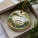 A decorative ornament in a box, featuring a scenic landscape with a cliff, trees, and a body of water.