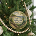 A round ornament hanging on a Christmas tree, featuring a scenic landscape with a bridge and trees.