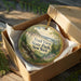 A decorative ornament in a brown box, featuring a scenic landscape with a bridge and trees, with the text "Trail View State Park, New York" prominently displayed.